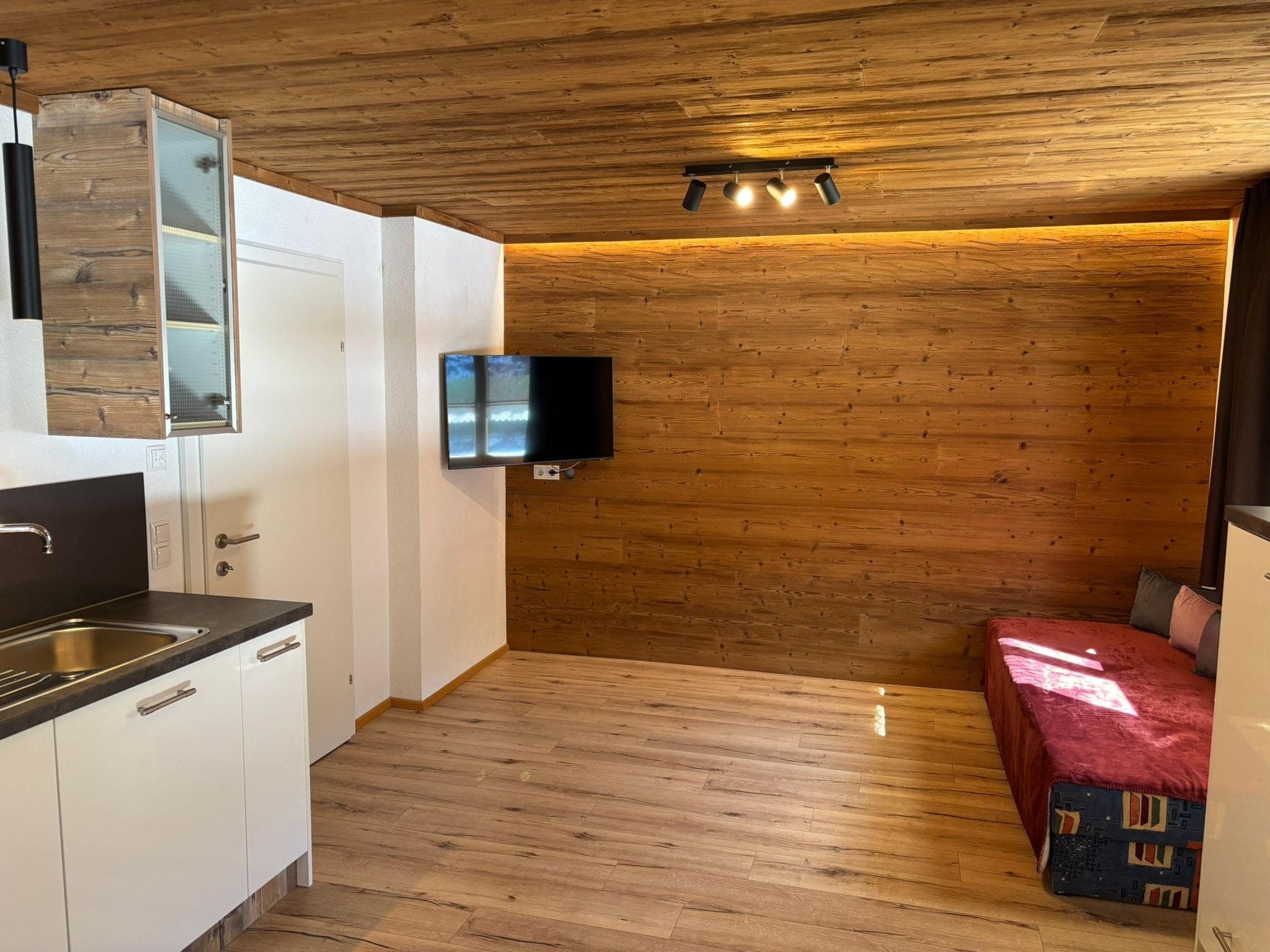 Bocks Apartments 61 - Top 3 Annabach - A spacious kitchen and dining area with wooden floors and a wooden ceiling. The kitchen features white cabinets and countertops, a built-in oven, and a coffee machine. A dark U-shaped banquette with a wooden table and chairs provides ample seating.